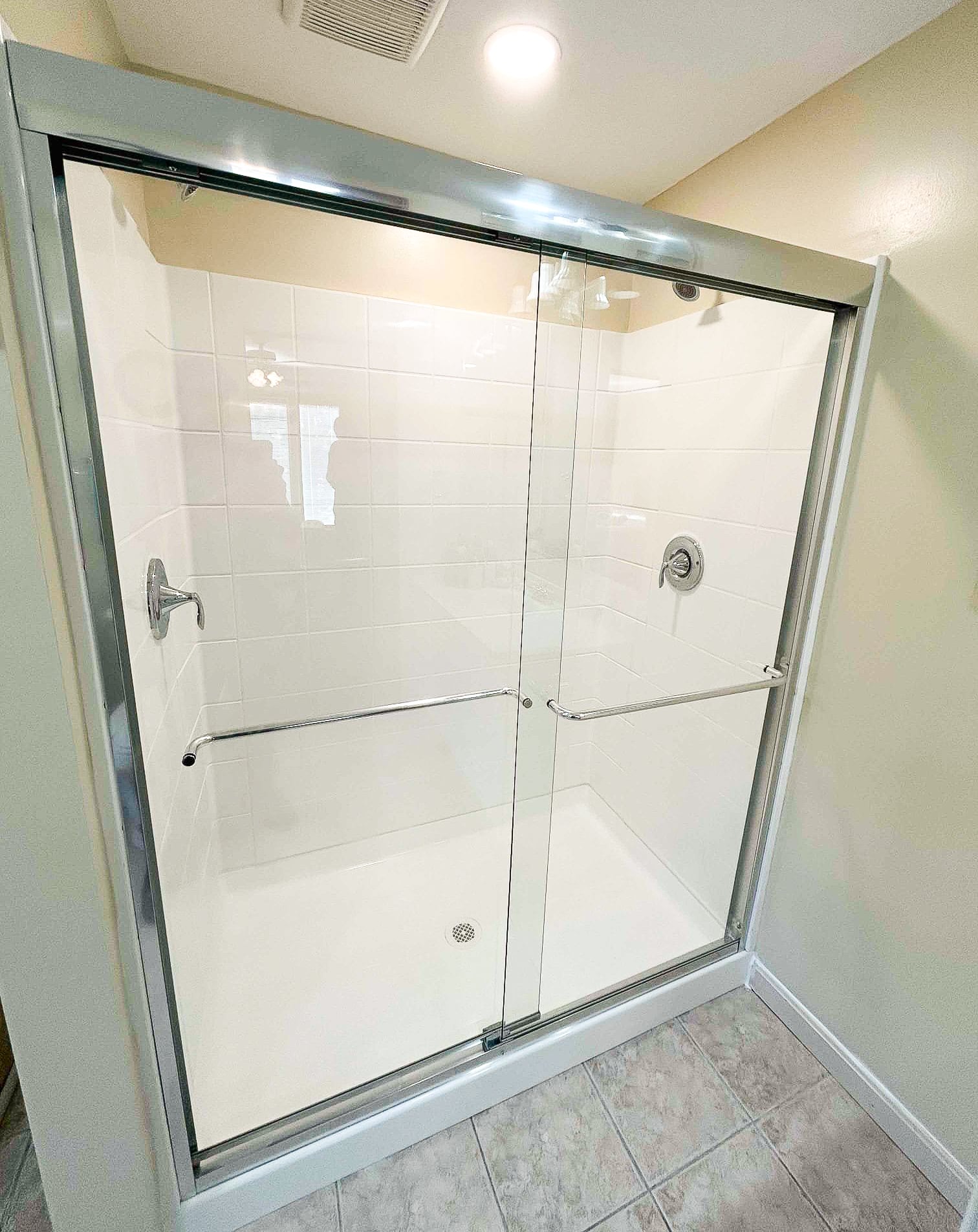 Clean white tile shower with frameless glass doors and dual showerheads — after Wahl remodel